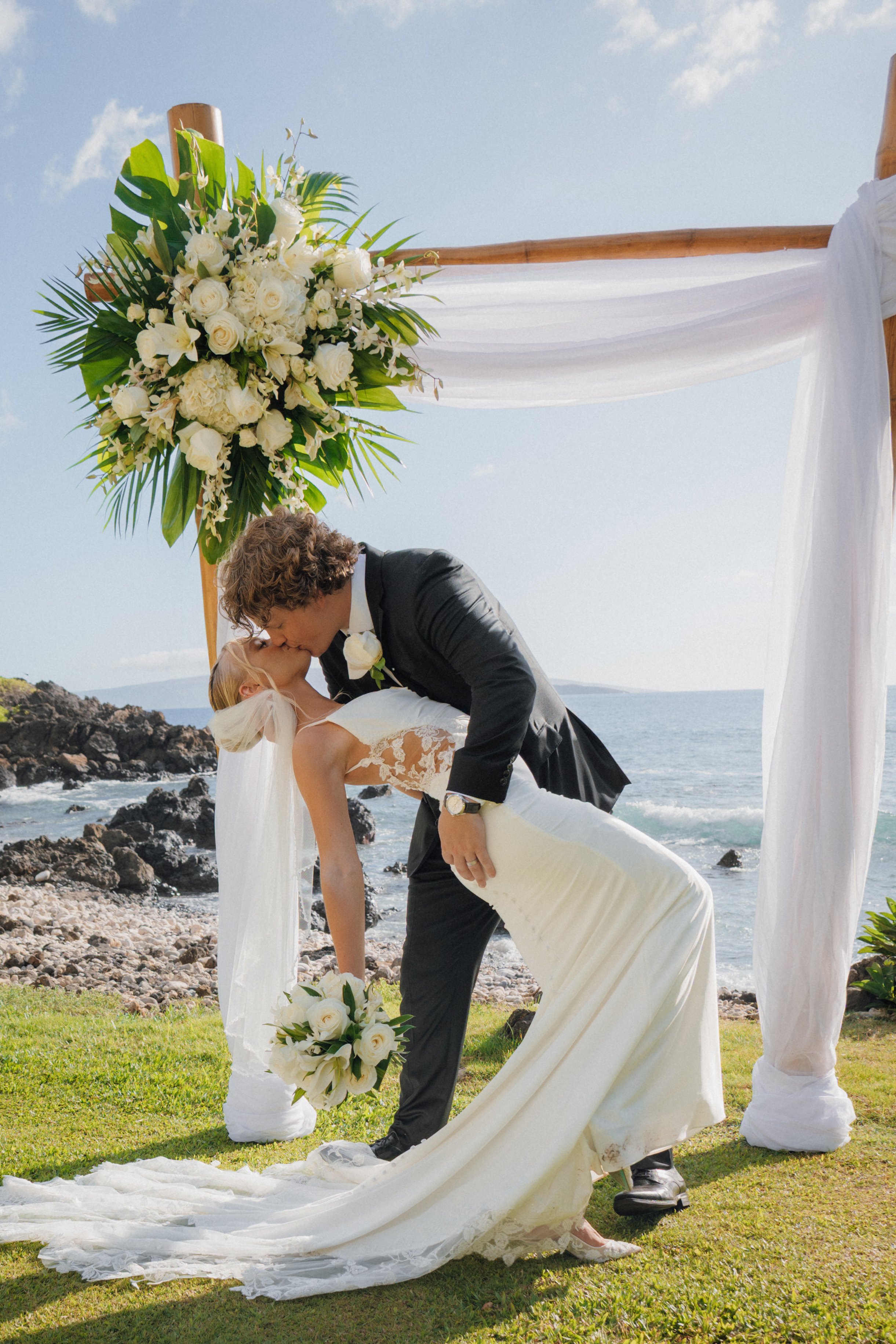 Couple kissing under a floral arch at a beach ceremony at Villa Vedas, Tabanan